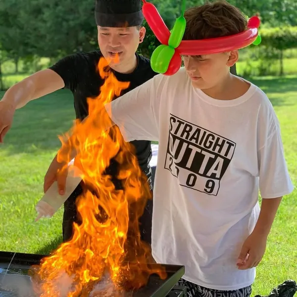 Hibachi chef doing a fire trick for a young guest at a backyard birthday party